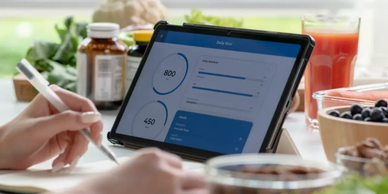 Person tracking calories and meals on a tablet surrounded by healthy foods.