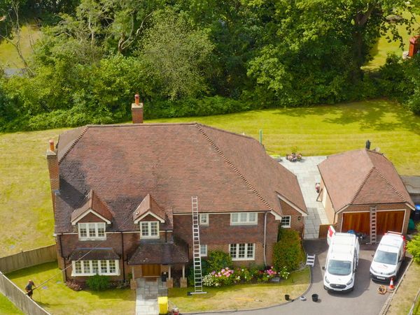A large brick house with two chimneys, a detached garage, and two white vans parked outside roof cleaning in progress.