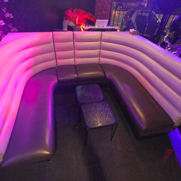 Curved lounge seating area with purple lighting and a DJ in the background.