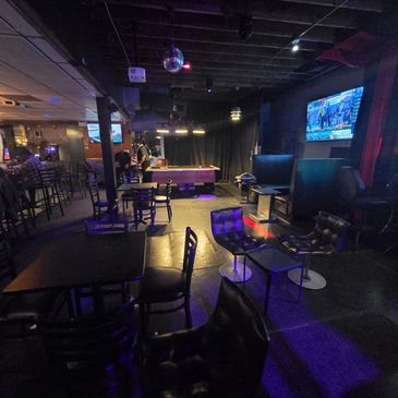 Dimly lit bar with pool table, chairs, and TV screens.