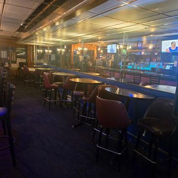 Empty bar area with round tables and bar stools under warm lighting.