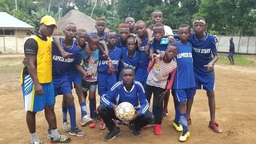 A group of young soccer players posing together on a dirt field.