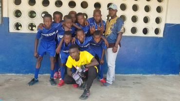 A youth soccer team posing in front of a blue and white wall.