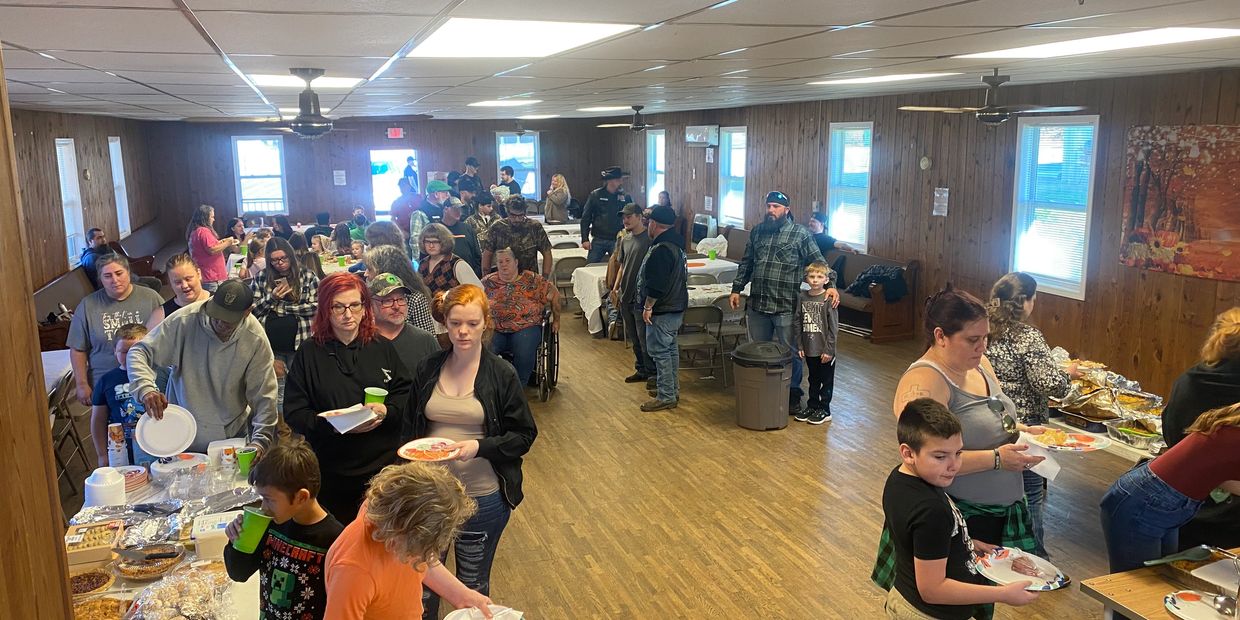 Community members lined up indoors for a shared meal in a cozy hall.