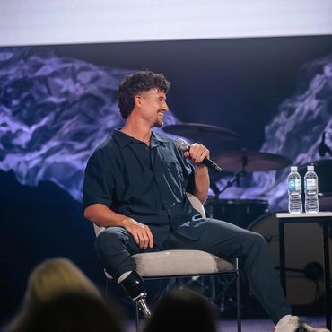 Trenten Merrill smiling onstage with a microphone during a speaking engagement.
