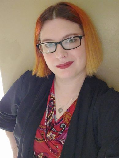 Picture of a Woman with red hair wearing a black jacket and red print shirt.