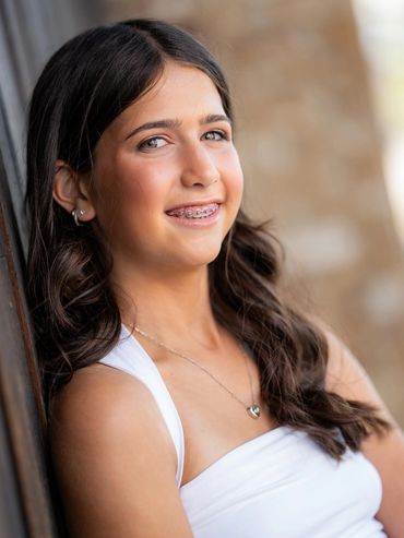 Teen girl with braces smiling and wearing a white top and heart necklace.