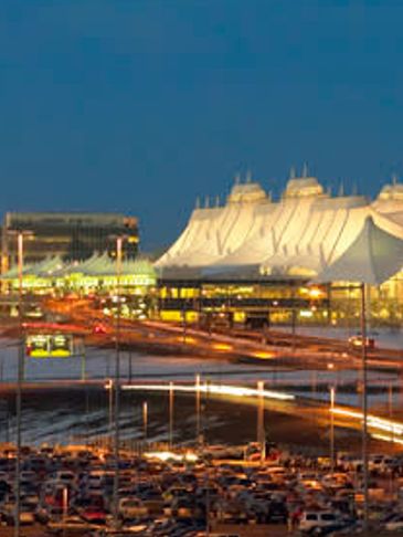 Night view of a large airport terminal with white tent-like roofing and busy traffic.