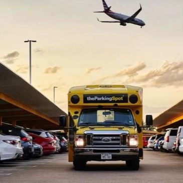 Yellow parking shuttle bus in a parking lot with a plane overhead.