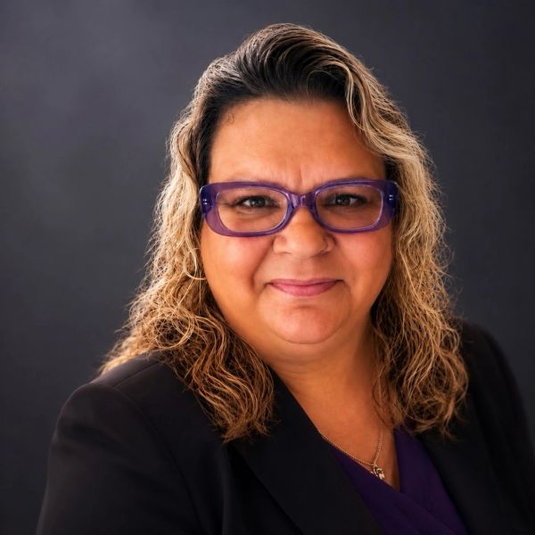 Smiling woman with purple glasses and wavy hair.