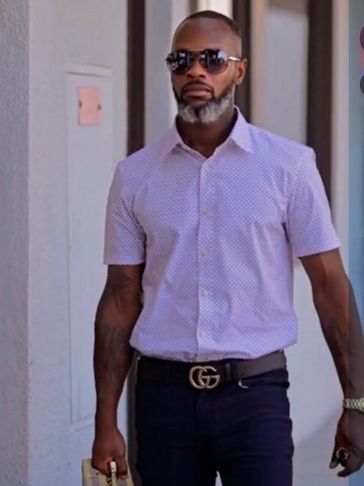Man with sunglasses wearing a light patterned shirt and dark pants.