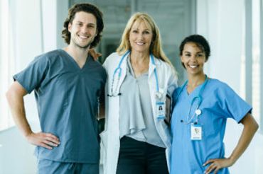 Three healthcare professionals smiling in a hospital corridor.