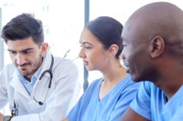 Three medical professionals collaborating over a laptop in a bright office.