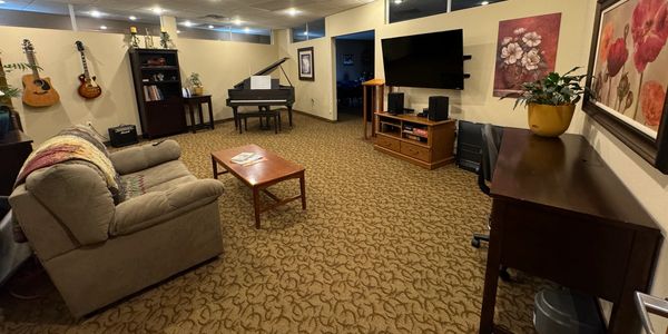 Experience Center with baby grand piano, guitars, sofa and plants, tv, stereo set up