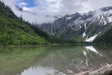 Glacier National Park - mini glacier area. Snowy mountains and waterfalls reflected in a serene lake with lush greenery.