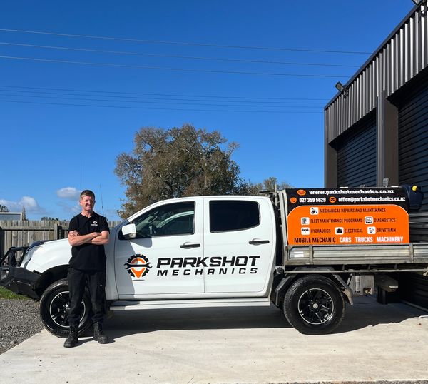 Man standing beside a Parkshot Mechanics service truck under clear blue sky.