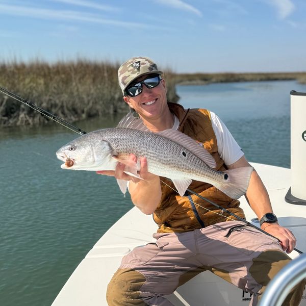 Man proudly holding a large fish on a boat in a calm waterway.