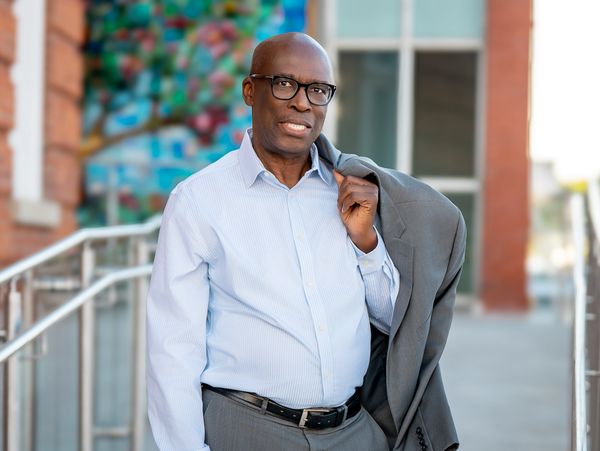 Confident man holding a jacket over his shoulder, standing outdoors.
