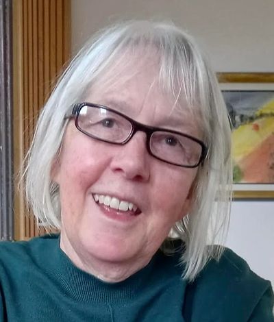 Jane Ricot is smiling at the camera, head tilted to her left. She wears glasses and is indoors.