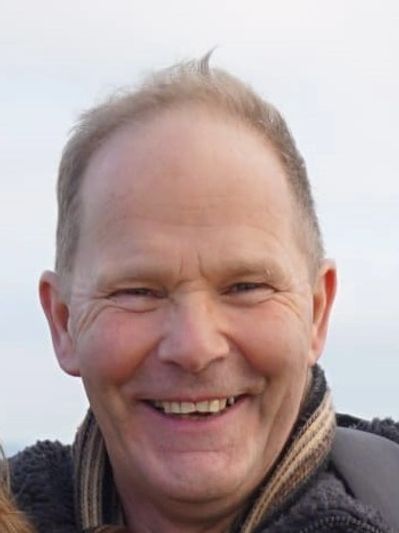 Martin Barker smiles cheerfully at the camera. He is outdoors. He is in a coat and scarf.