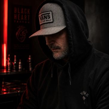 Man in a hooded sweatshirt and Vans cap in moody lighting.