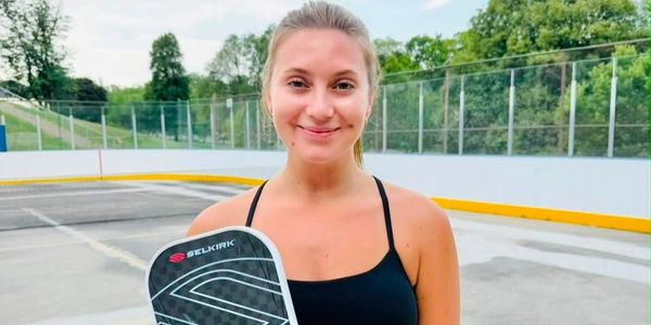 Young woman holding a pickleball paddle outdoors.