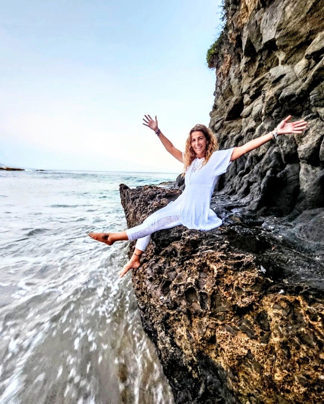 Woman in white dress sitting on a rocky shore by the sea.