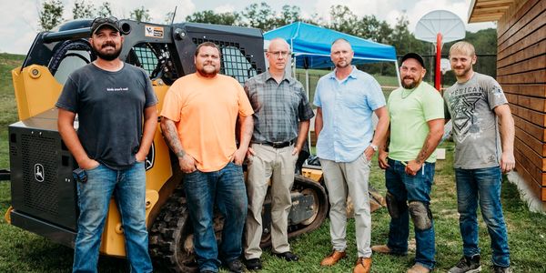 Our crew of seasoned professionals pose in front of a small bulldozer.