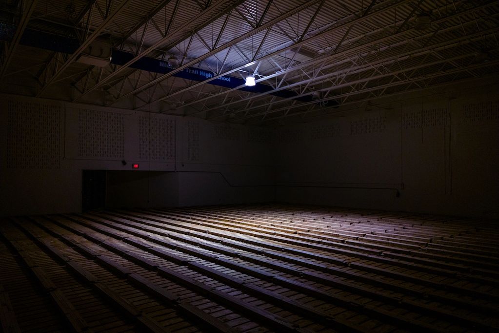 A high school gym under renovation is lit by a lone bulb. 