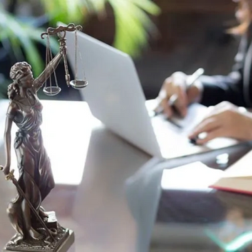 Lady Justice statue beside a person working on a laptop and writing notes.