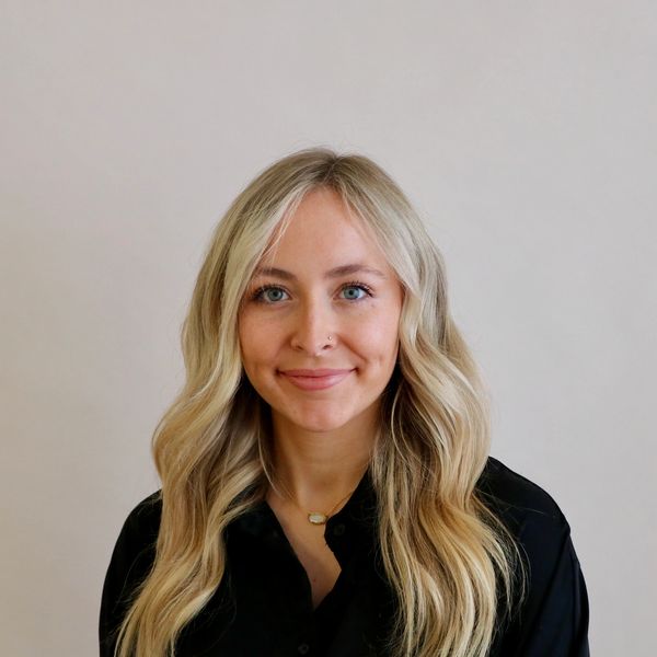 Smiling woman with long blonde hair and blue eyes against a plain background.