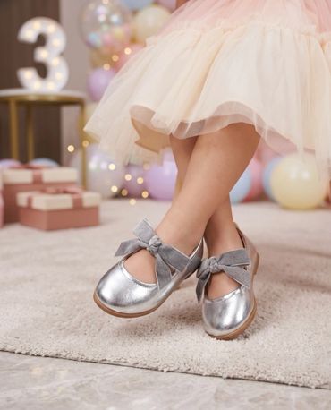 Child wearing silver shoes with gray bows and a cream tutu skirt.