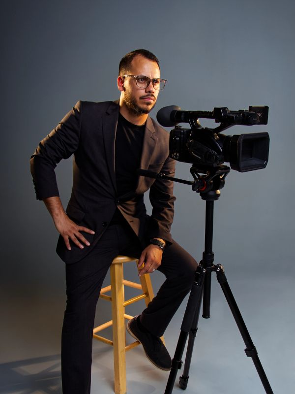 Man in black suit operating video camera on tripod.