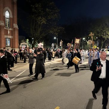 Nighttime procession with people carrying religious banners and playing drums.