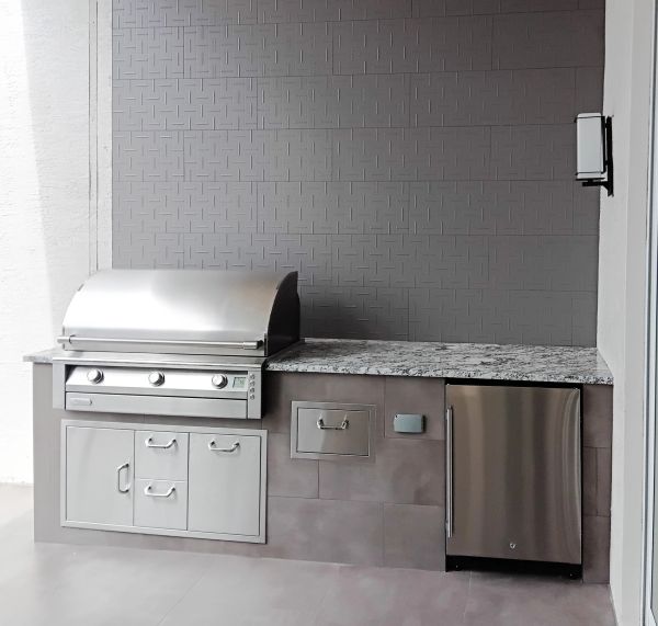 Modern outdoor kitchen with stainless steel grill and refrigerator.