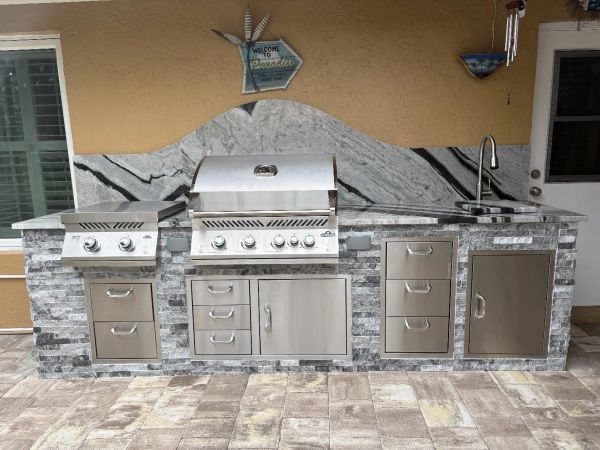 Modern outdoor kitchen with stainless steel grill and storage under a marble countertop.
