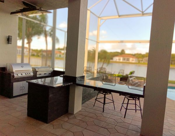 Outdoor kitchen with grill and seating by a lake.