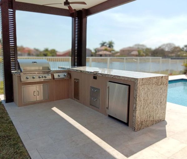 Modern outdoor kitchen with grill and refrigerator by the pool.