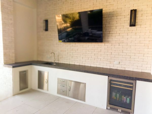 Modern outdoor kitchen with TV, sink, and mini fridge on a brick wall.
