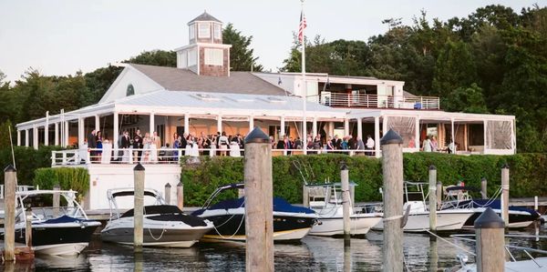 Boats docked near a waterfront building with people gathered on the porch.