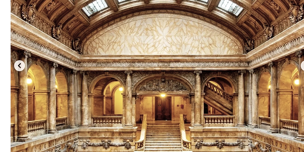 Grand marble staircase in an ornate historic building with a glass ceiling.