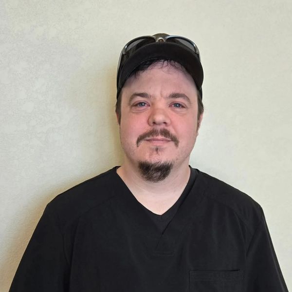 Man in black shirt and cap with sunglasses on head.