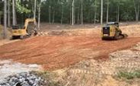 Construction vehicles grading a cleared, dirt-covered forest area.