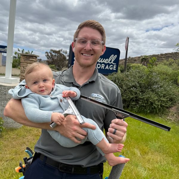 Man holding baby and window cleaning tool outside on a cloudy day.