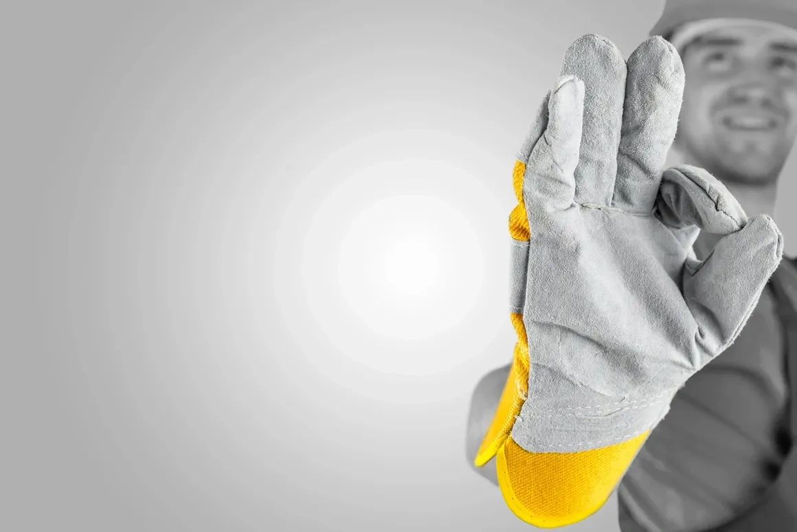 Construction worker showing a grey and yellow protective glove in an OK gesture.