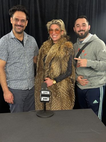 Three smiling individuals stand behind a microphone labeled Community News Network.