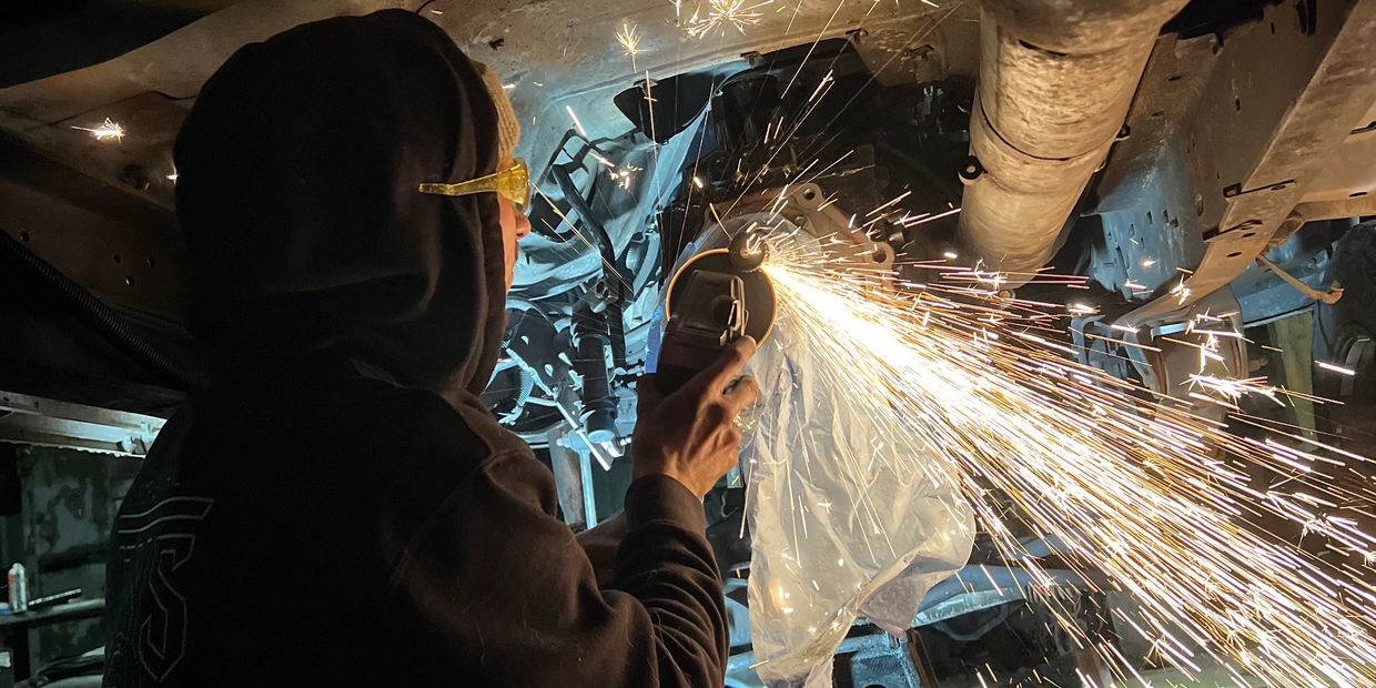 Person grinding metal under a vehicle, sparks flying.