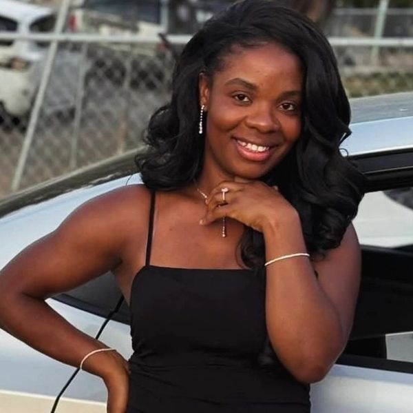Smiling woman in a black dress posing by a car outdoors.