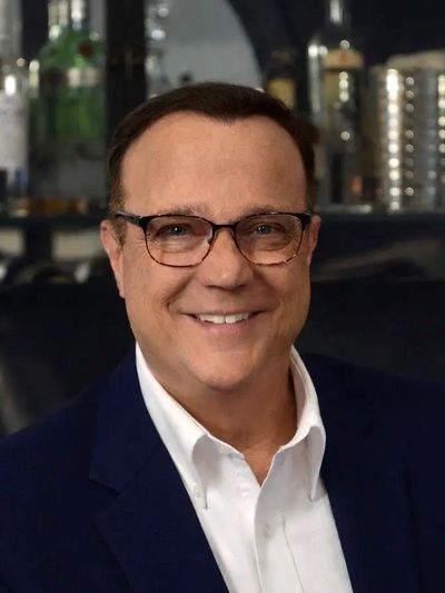 Smiling man with glasses wearing a navy blue blazer and white shirt.