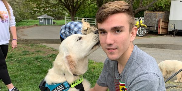 A young man with a service dog outdoors in a park setting.